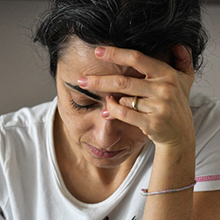 A woman looks down seemingly distressed while holding her hand to her forehead